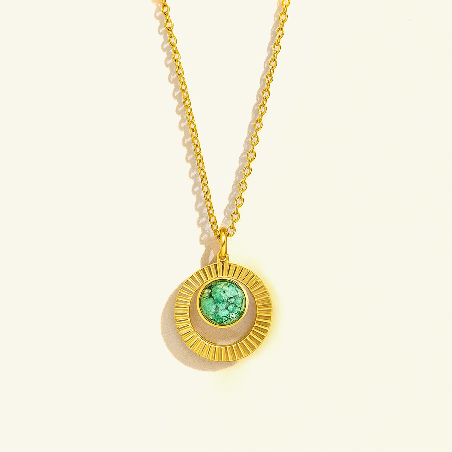 Gold necklace with a green gemstone pendant on a light beige background